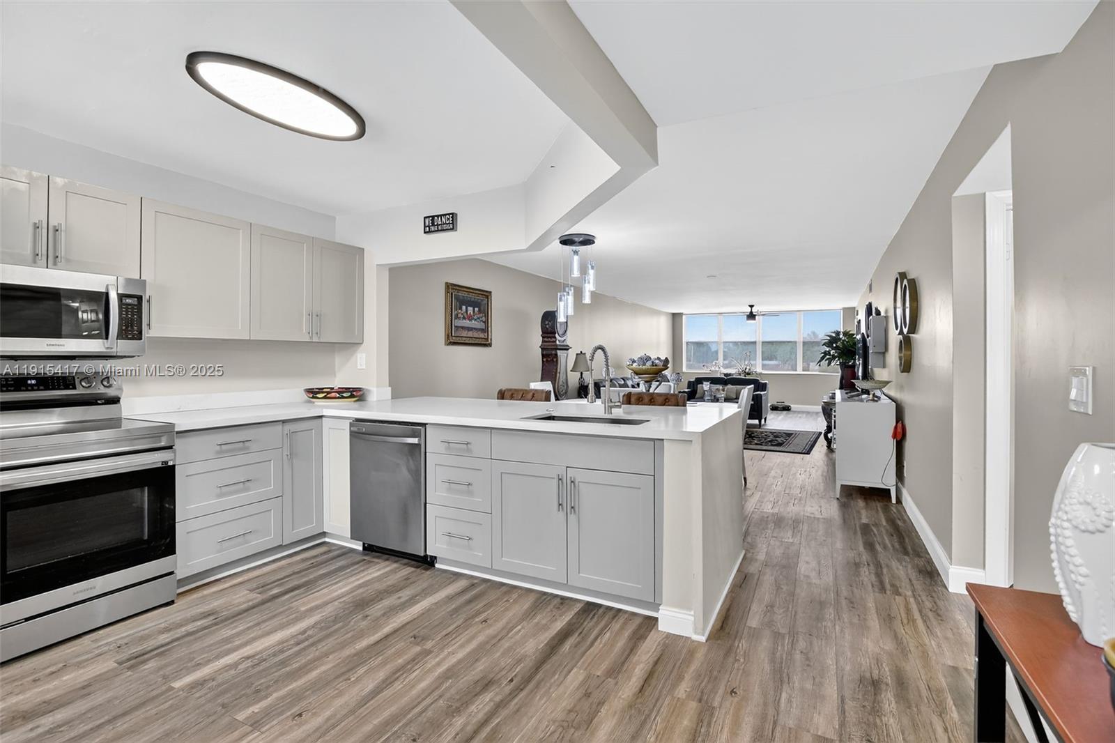 A modern kitchen with light gray cabinets and stainless steel appliances opens to a living area — 2521 NW 104th Ave # 203, Sunrise FL 33322, SUNRISE, FL