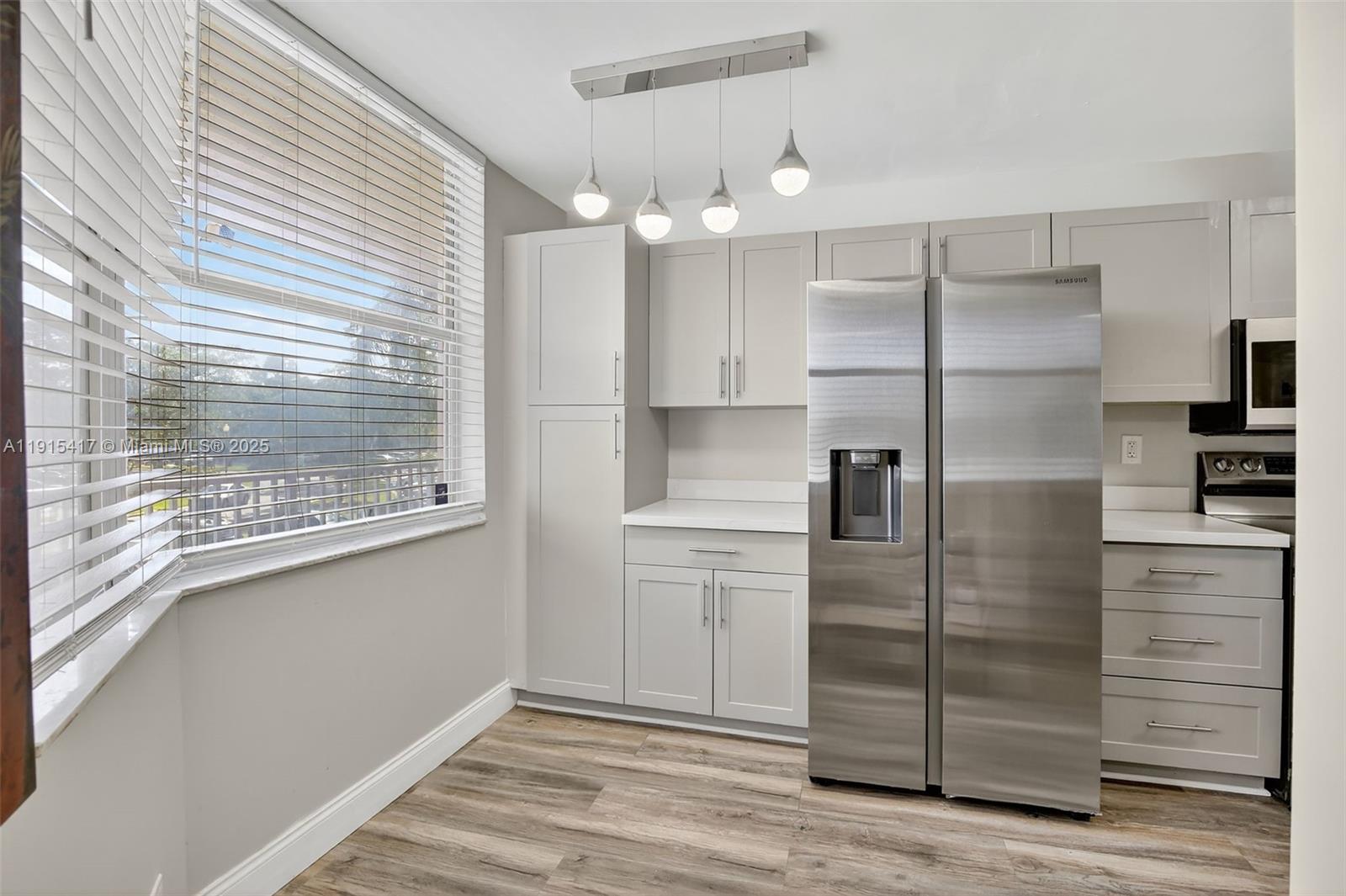 A kitchen features light gray cabinets, stainless steel appliances, and wood-look flooring near a window — 2521 NW 104th Ave # 203, Sunrise FL 33322, SUNRISE, FL