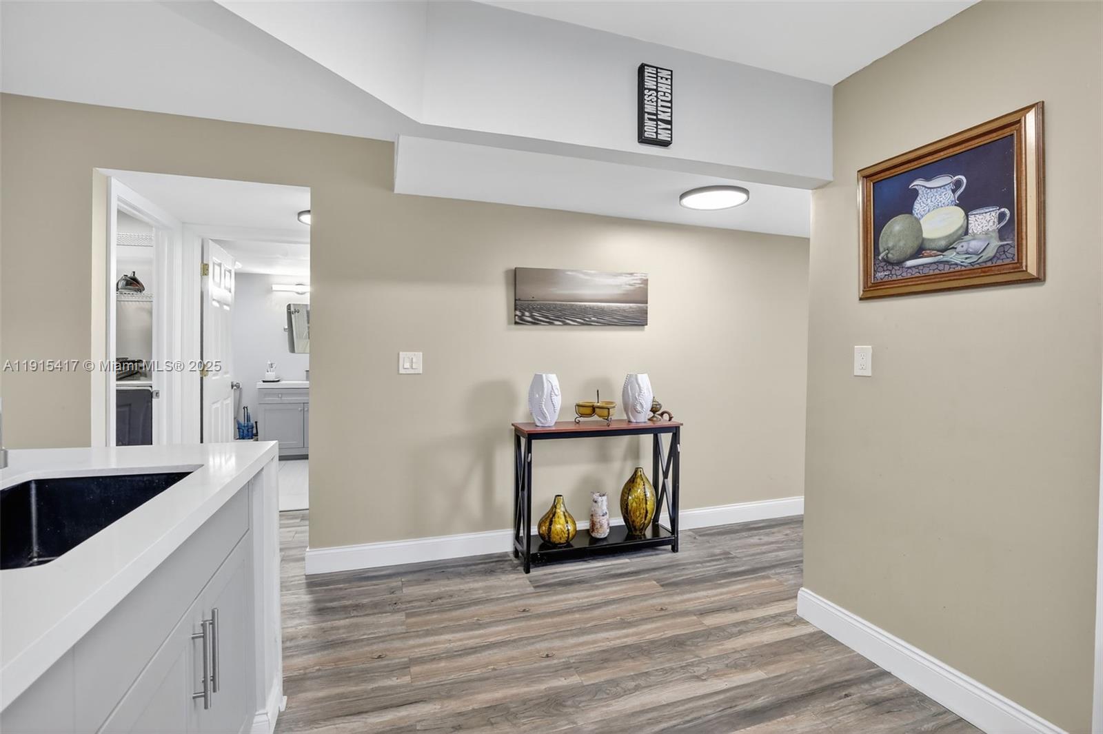 A hallway with wood-look flooring leads to a bathroom, featuring a console table and artwork — 2521 NW 104th Ave # 203, Sunrise FL 33322, SUNRISE, FL