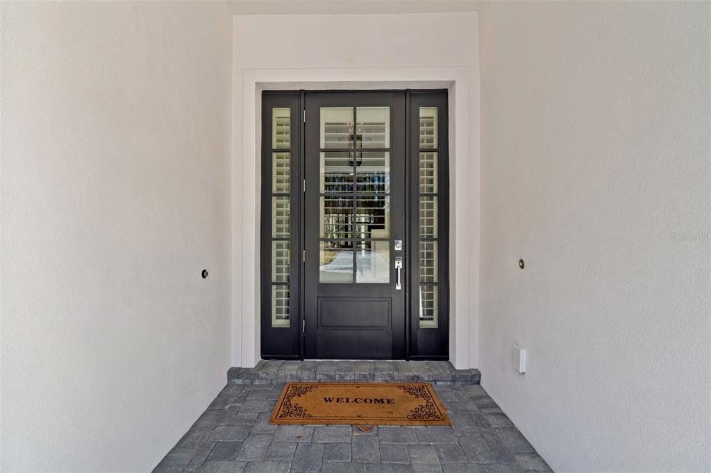 A dark-framed front door with glass panels and sidelights sits on a paved entryway — 4905 MAJESTIC HILLS LOOP, BROOKSVILLE, FL