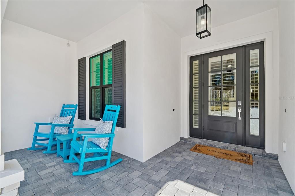 A covered front porch features gray paver flooring, two bright blue rocking chairs, and a dark-framed door — 4905 MAJESTIC HILLS LOOP, BROOKSVILLE, FL