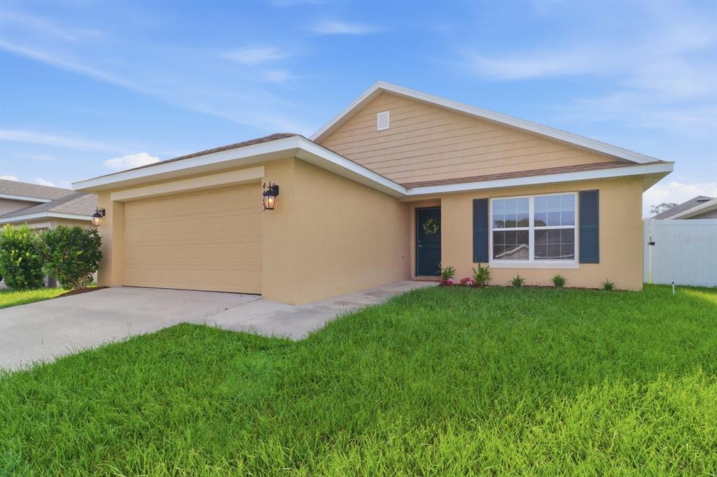 A single-story house with a tan stucco exterior, a two-car garage, and a front lawn — 4493 NW 2ND COURT, OCALA, FL