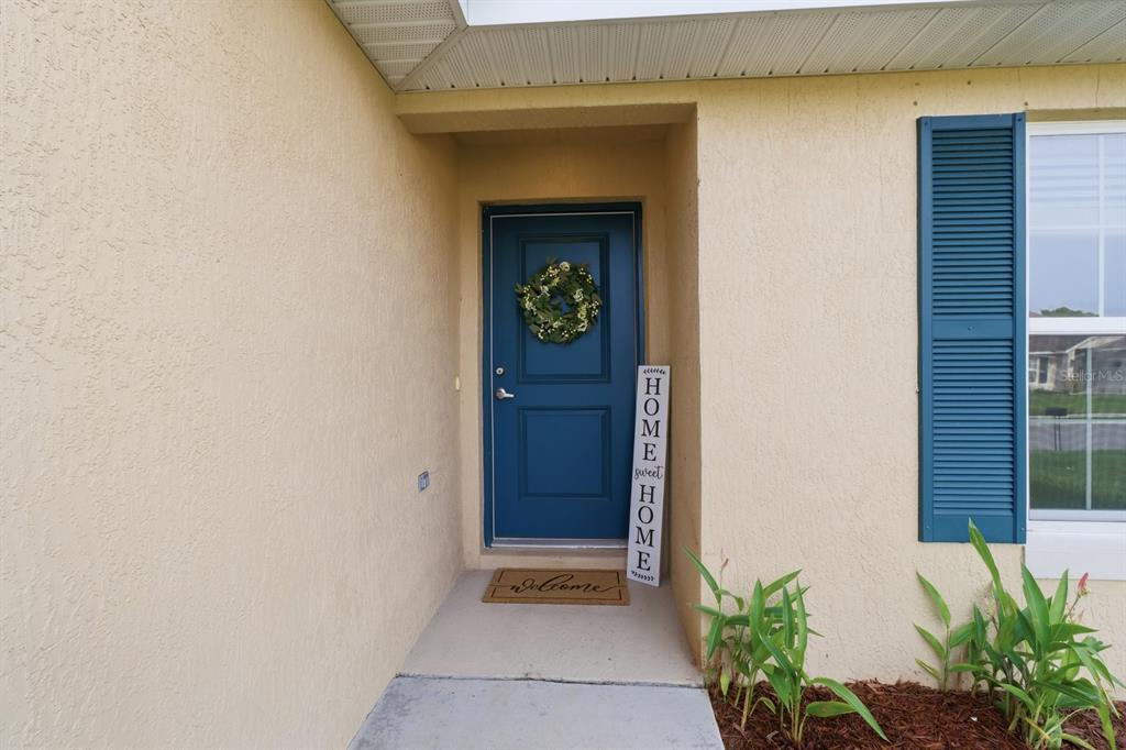 A blue front door with a wreath and a welcome sign sits under a porch — 4493 NW 2ND COURT, OCALA, FL
