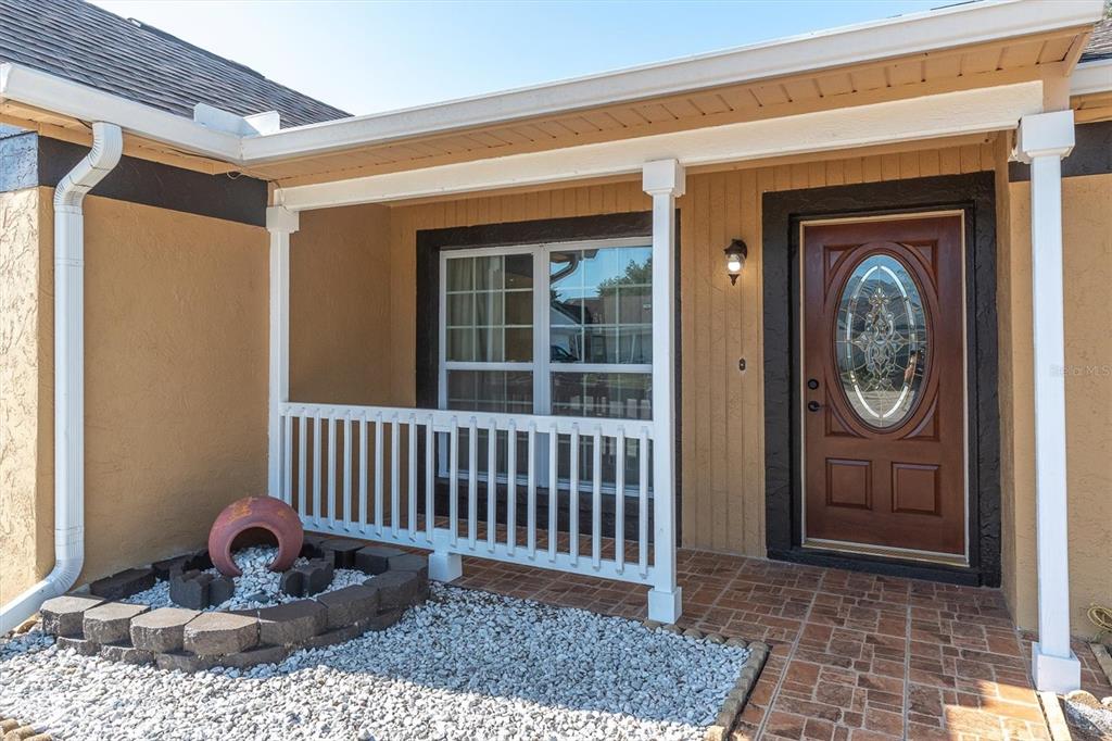 A tan house exterior features a covered porch, a brown front door, and a rock garden — 6832 SWAIN AVENUE, TAMPA, FL
