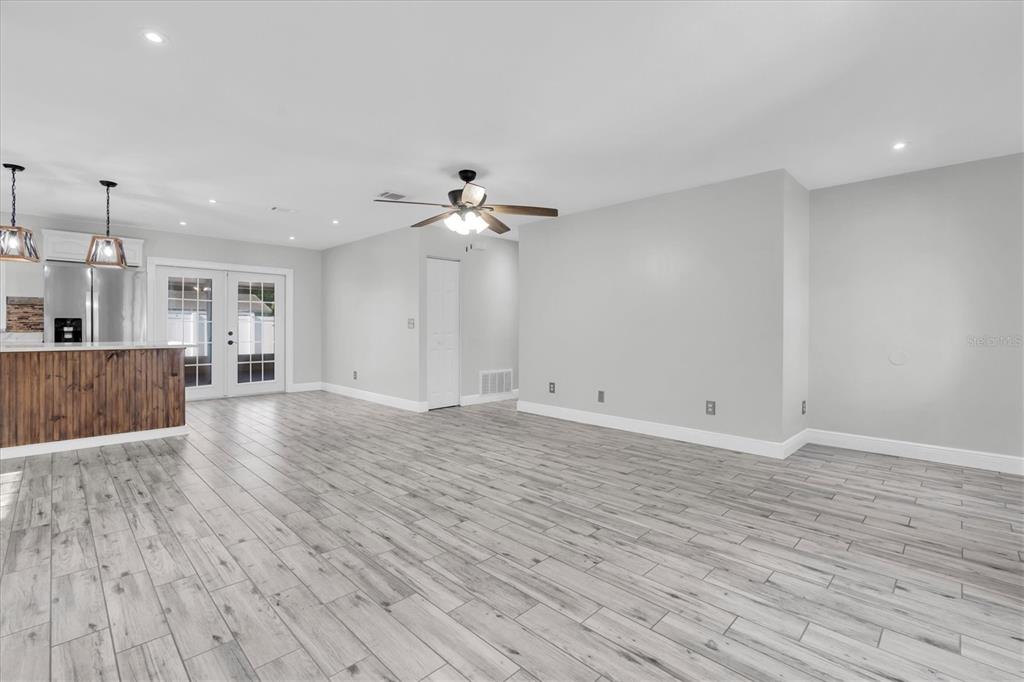 A spacious living area with light wood-look tile flooring, a ceiling fan, and kitchen access — 6832 SWAIN AVENUE, TAMPA, FL
