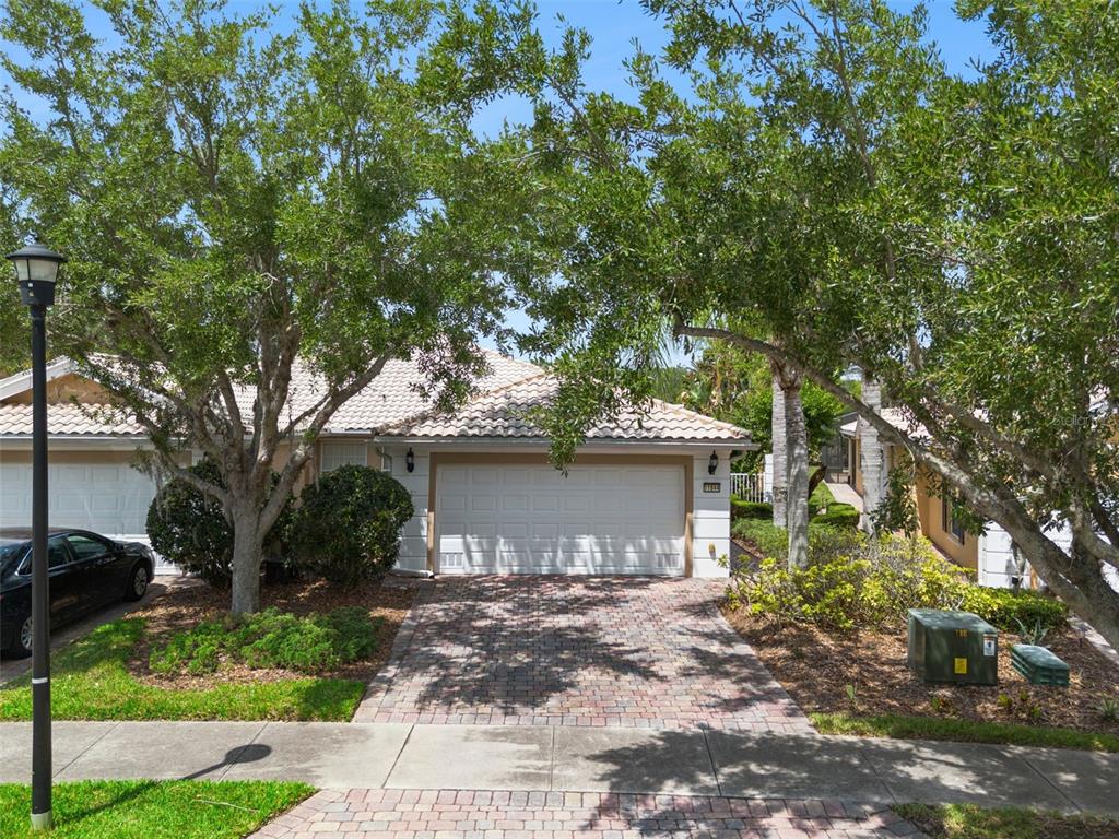 A single-story house with a white garage door, tiled roof, and brick driveway — 11844 ASTILBE DRIVE, ORLANDO, FL