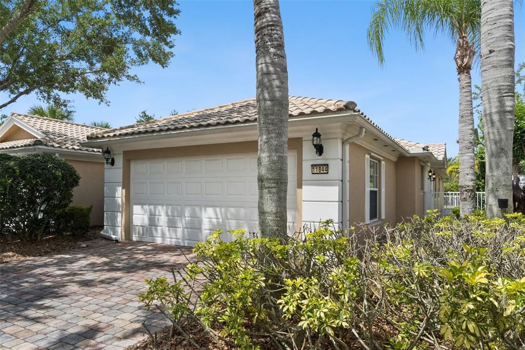 A tan house exterior features a white garage door, a tiled roof, and palm trees — 11844 ASTILBE DRIVE, ORLANDO, FL