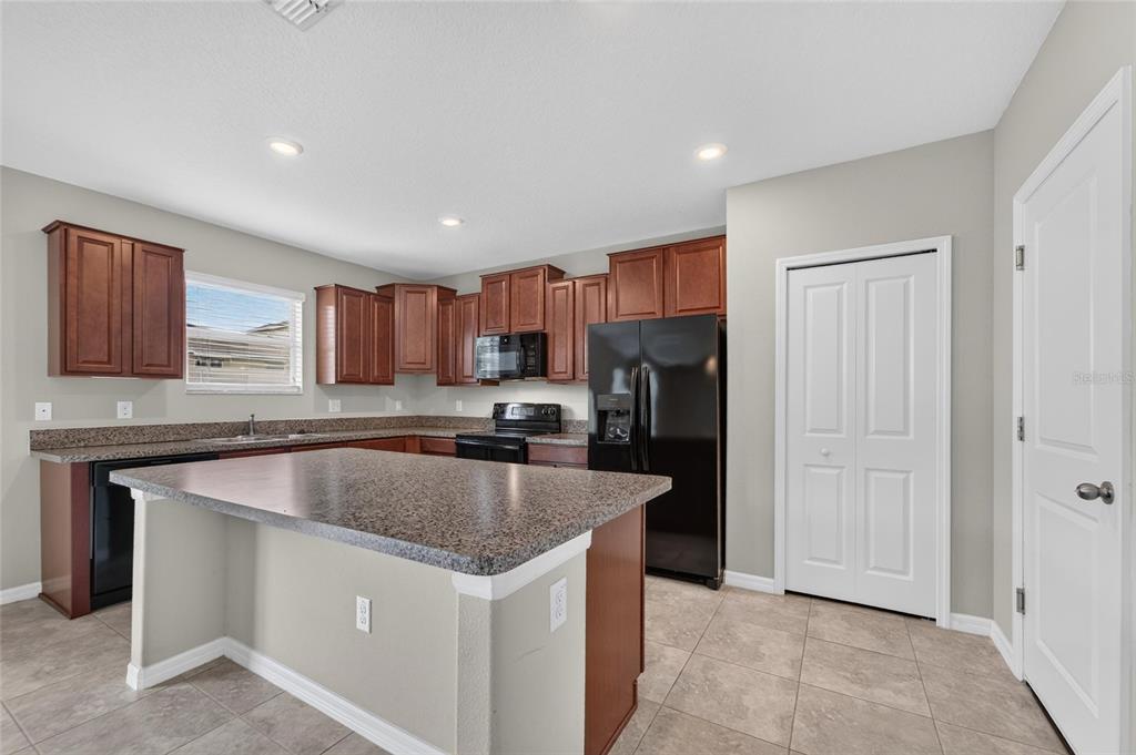 A kitchen features brown cabinets, granite countertops, a center island, and black appliances — 215 ENGLISH HERITAGE PLACE, DOVER, FL