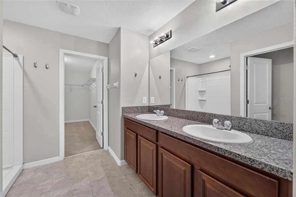 A bathroom with a double-sink granite vanity, wood cabinets, and an adjacent walk-in closet — 215 ENGLISH HERITAGE PLACE, DOVER, FL