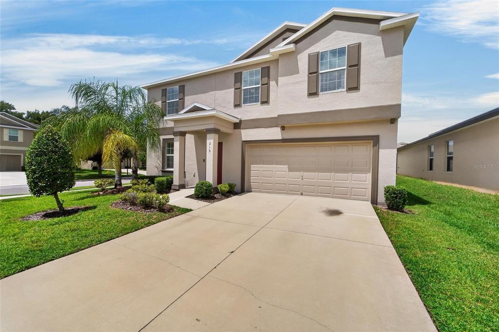 A two-story suburban house features a beige stucco exterior, a two-car garage, and landscaping — 215 ENGLISH HERITAGE PLACE, DOVER, FL