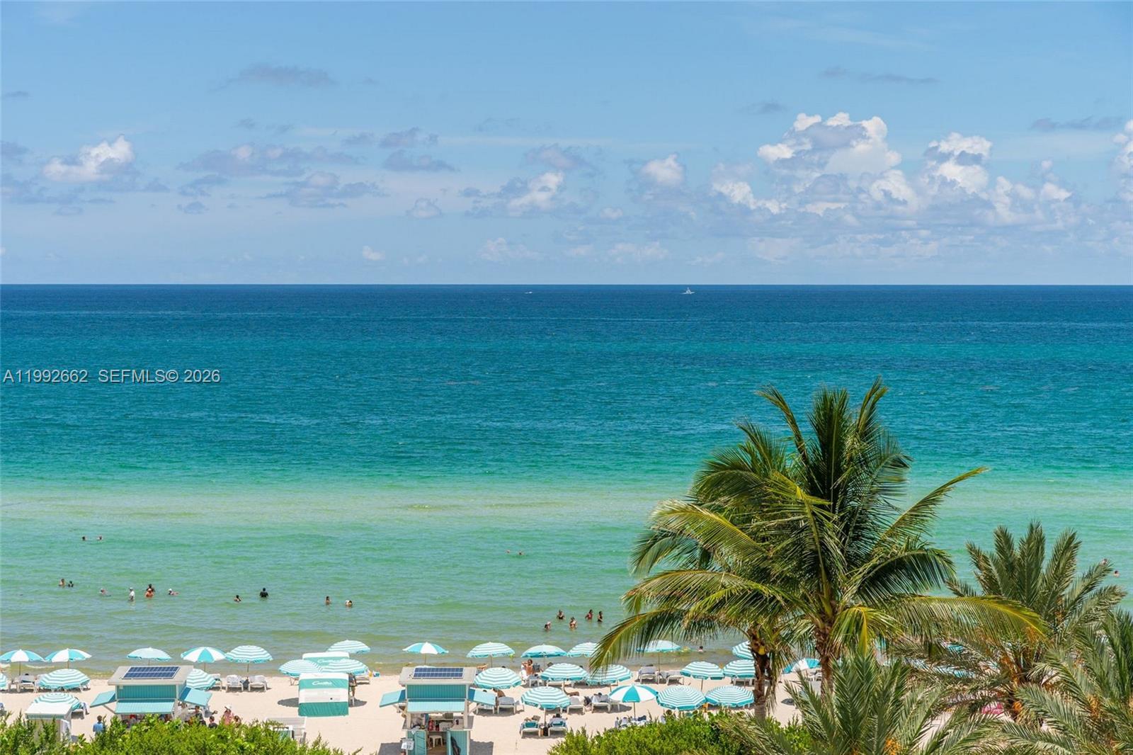 An elevated view of a sandy beach with blue umbrellas and palm trees — 6801 Collins Ave # 1414, Miami Beach FL 33141, MIAMI BEACH, FL