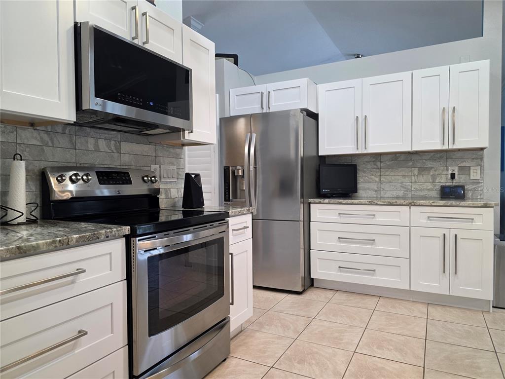 A kitchen features white cabinets, stainless steel appliances, and gray tile backsplash — 95 SPORTSMAN ROAD, ROTONDA WEST, FL