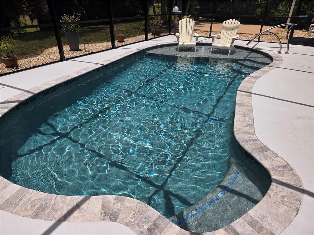 A swimming pool with a sun shelf and two chairs sits inside a screened enclosure — 95 SPORTSMAN ROAD, ROTONDA WEST, FL