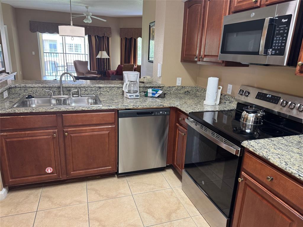 A kitchen features wood cabinets, granite countertops, stainless steel appliances, and tile flooring — 8762 WORLDQUEST BOULEVARD UNIT 6203, ORLANDO, FL