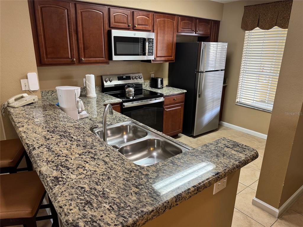 A kitchen features dark wood cabinets, granite countertops, stainless steel appliances, and a double sink — 8762 WORLDQUEST BOULEVARD UNIT 6203, ORLANDO, FL