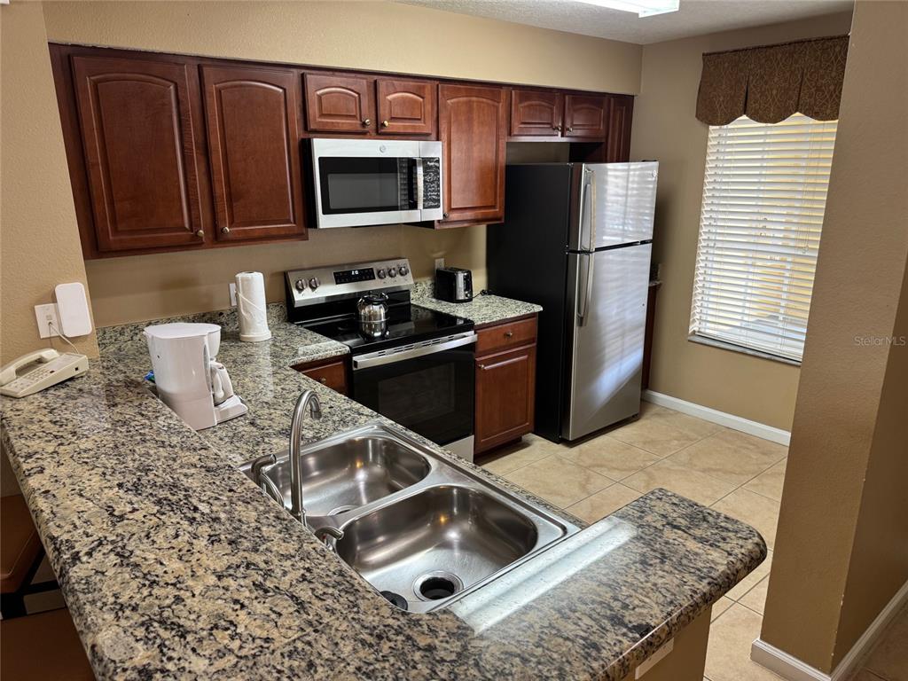 A kitchen features dark wood cabinets, granite countertops, stainless steel appliances, and a double sink — 8762 WORLDQUEST BOULEVARD UNIT 6203, ORLANDO, FL