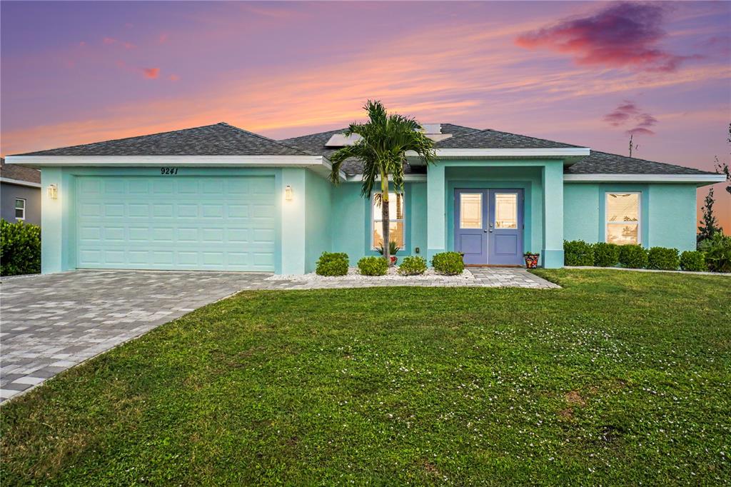 A light blue single-story house with a two-car garage and a paved driveway at sunset — 9241 KING HILL STREET, PORT CHARLOTTE, FL