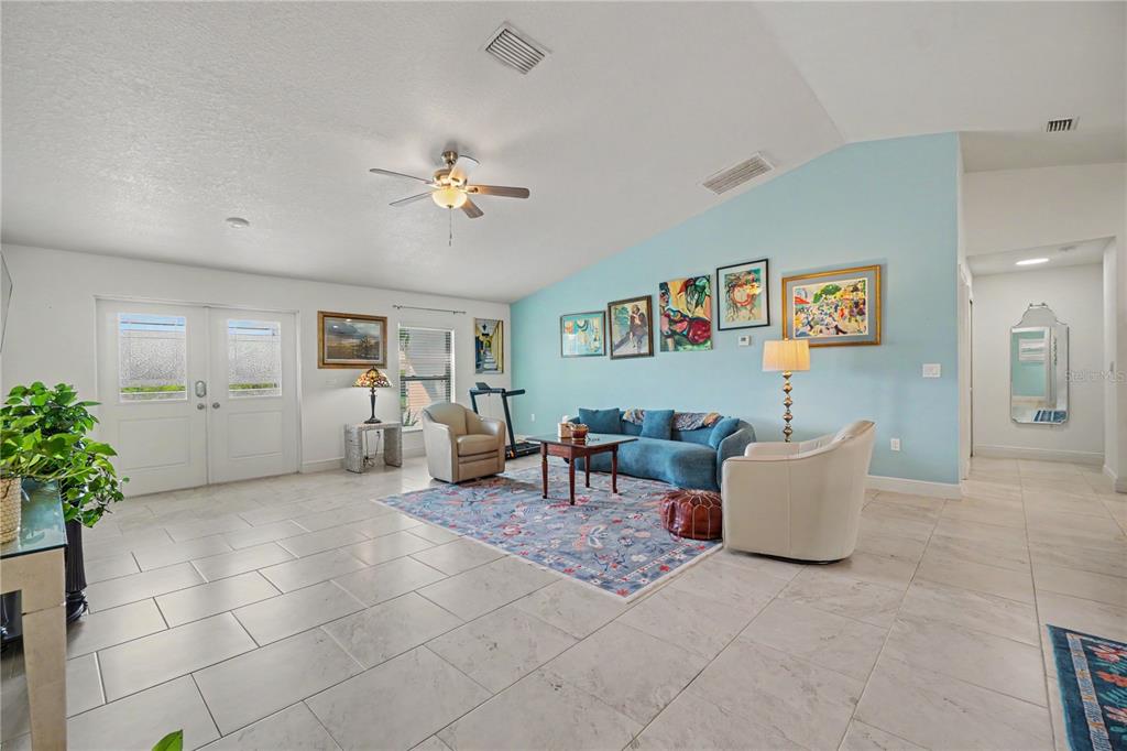 A spacious living room features light blue walls, tile flooring, a vaulted ceiling, and furniture — 9241 KING HILL STREET, PORT CHARLOTTE, FL