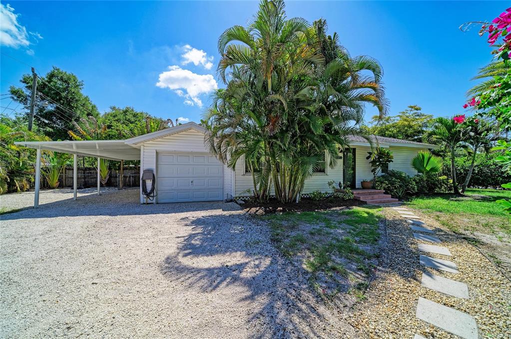 A single-story house with white siding, a gravel driveway, a carport, and a large palm tree — 3710 RILMA AVENUE, SARASOTA, FL