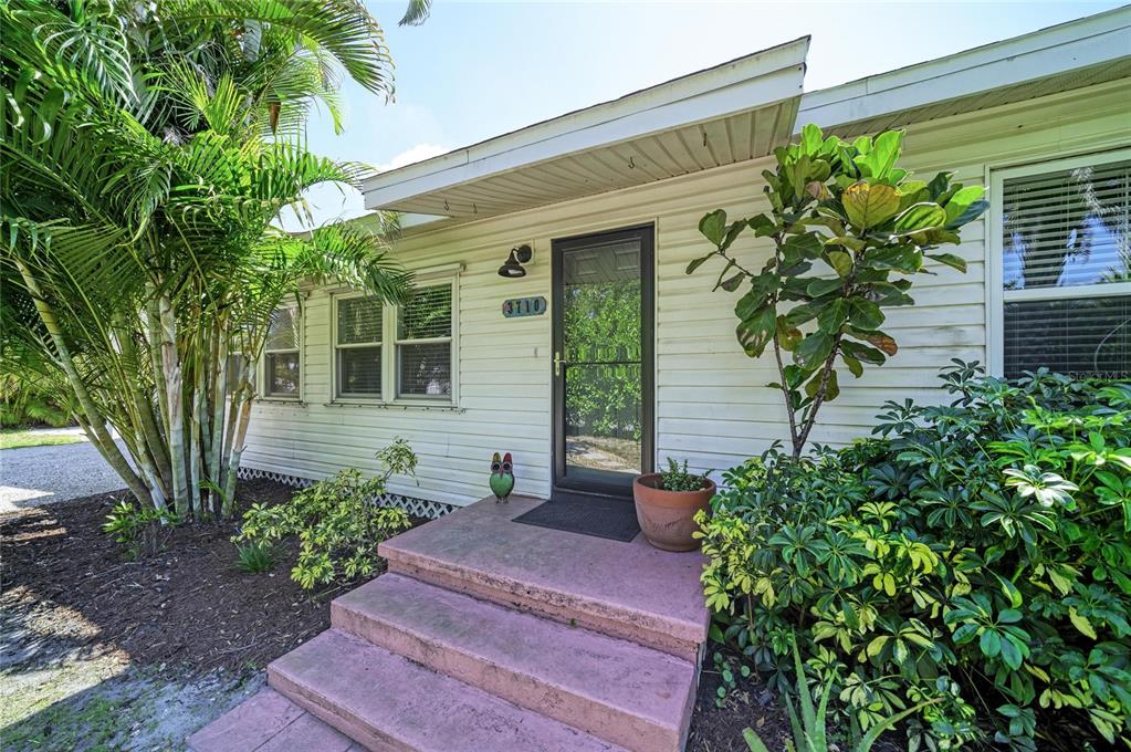 A white-sided house exterior features a front door with a storm door and pink steps — 3710 RILMA AVENUE, SARASOTA, FL