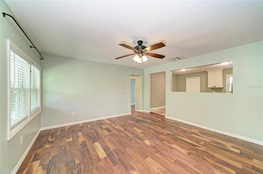An empty living room features light green walls, dark wood-look flooring, and a ceiling fan — 3710 RILMA AVENUE, SARASOTA, FL
