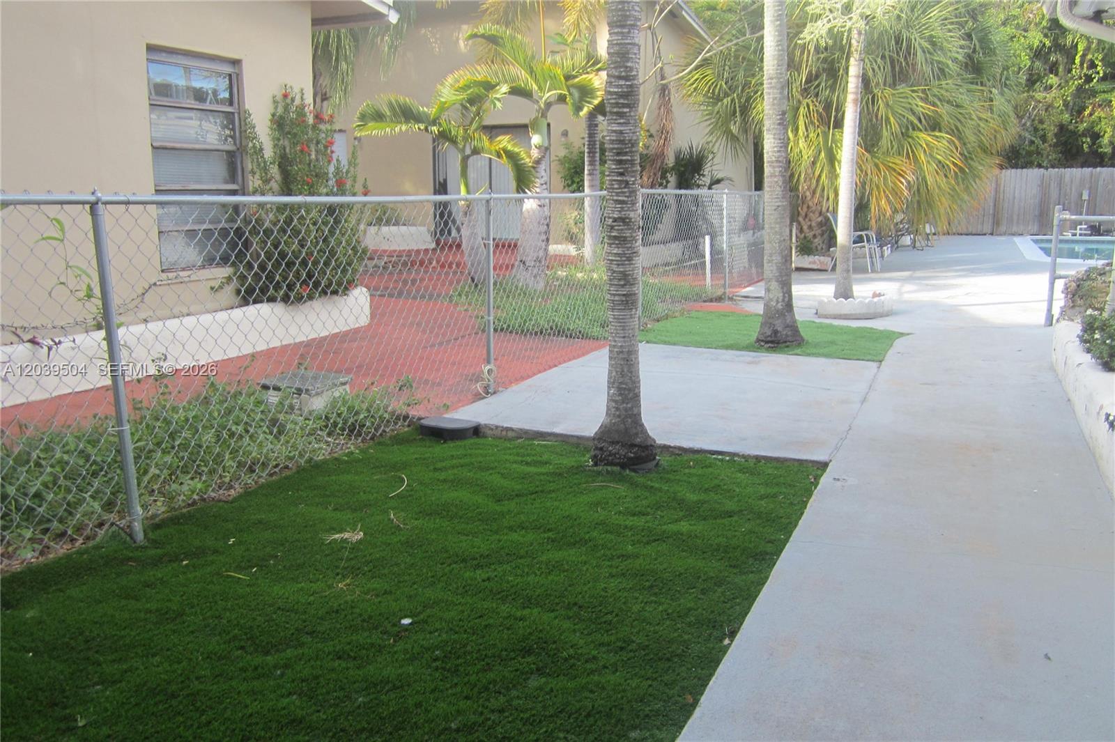 A chain-link fence separates a grassy area and concrete walkway from a patio space — HOLLYWOOD, FL