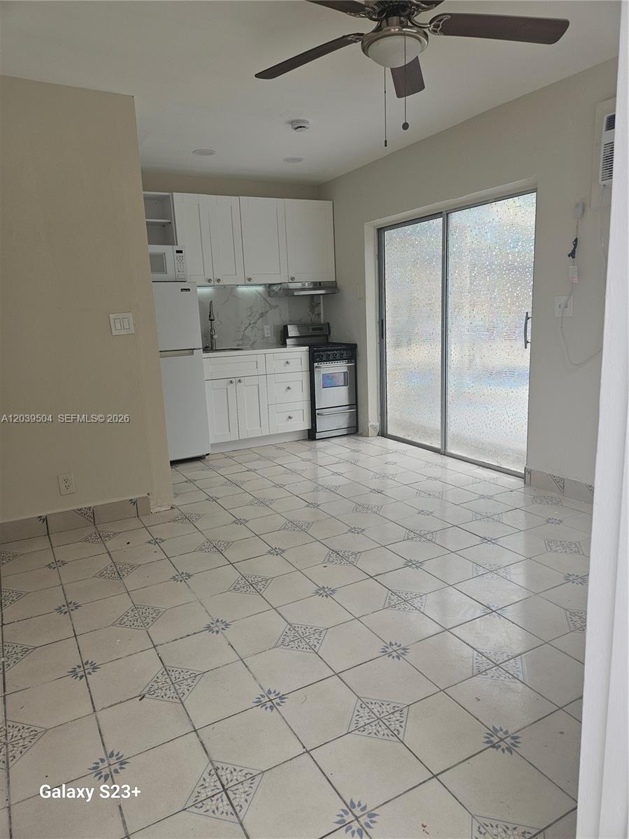 A kitchen features white cabinets, a stainless steel stove, and tiled floors near sliding doors — HOLLYWOOD, FL
