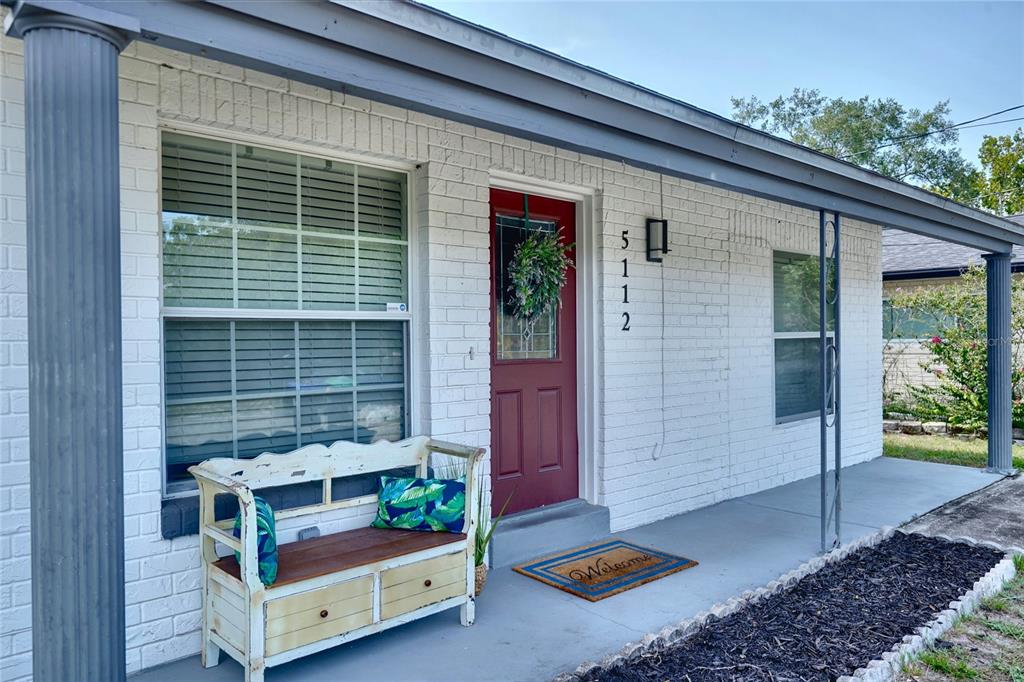 A white brick house exterior features a red front door, a porch bench, and columns — 5112 GLASGOW AVENUE, ORLANDO, FL