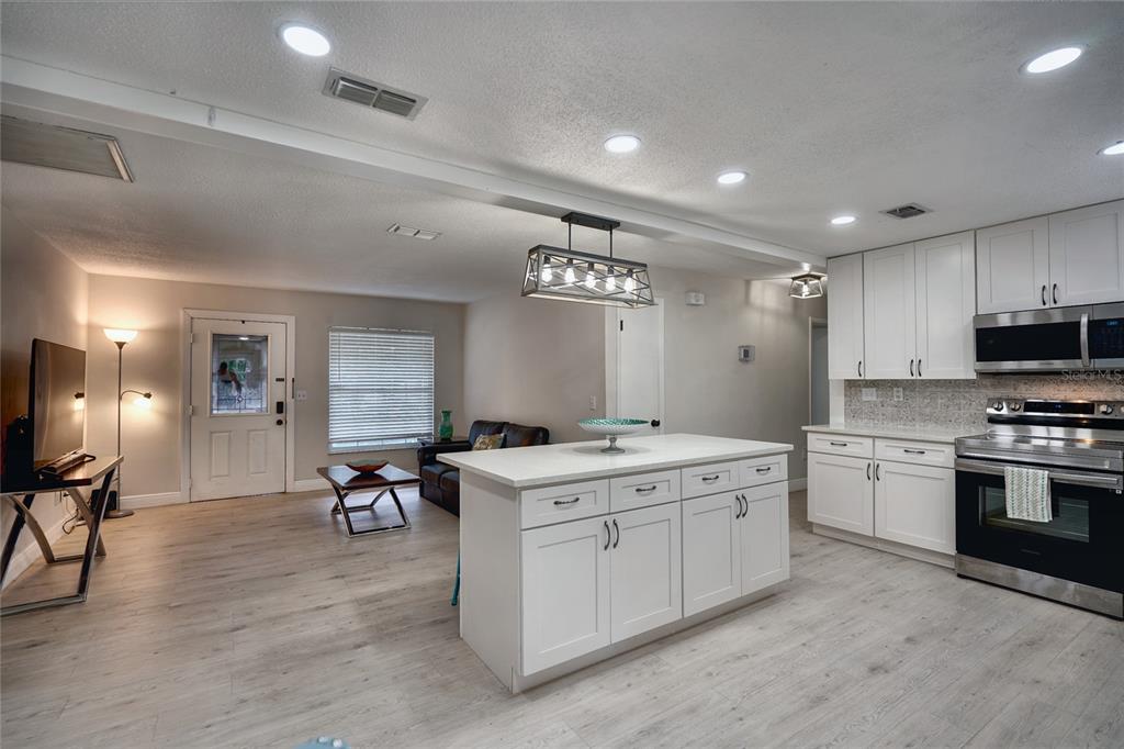 An open-concept kitchen and living area features white cabinetry, a central island, and light flooring — 5112 GLASGOW AVENUE, ORLANDO, FL