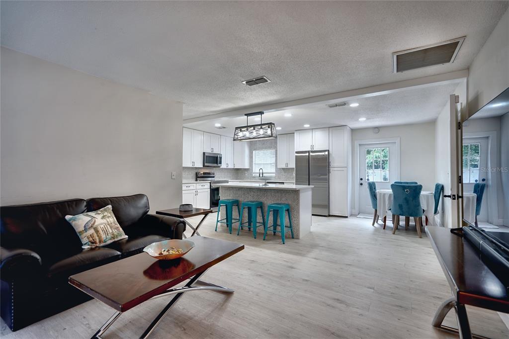An open-concept kitchen and living area features white cabinetry, a granite island, and teal stools — 5112 GLASGOW AVENUE, ORLANDO, FL