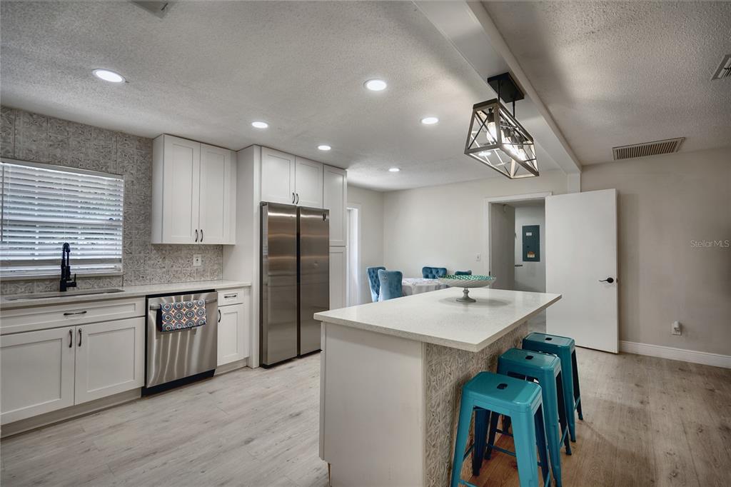 A modern kitchen features white cabinets, stainless steel appliances, a center island, and teal stools — 5112 GLASGOW AVENUE, ORLANDO, FL