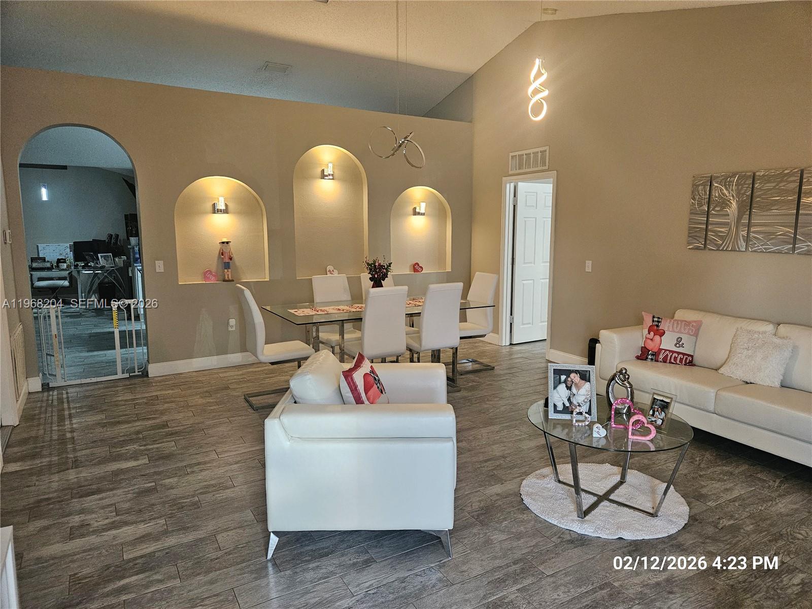 A living and dining area features arched wall niches, white furniture, and wood-look tile flooring — 3046 Blaine Cir, Deltona FL 32738, DELTONA, FL