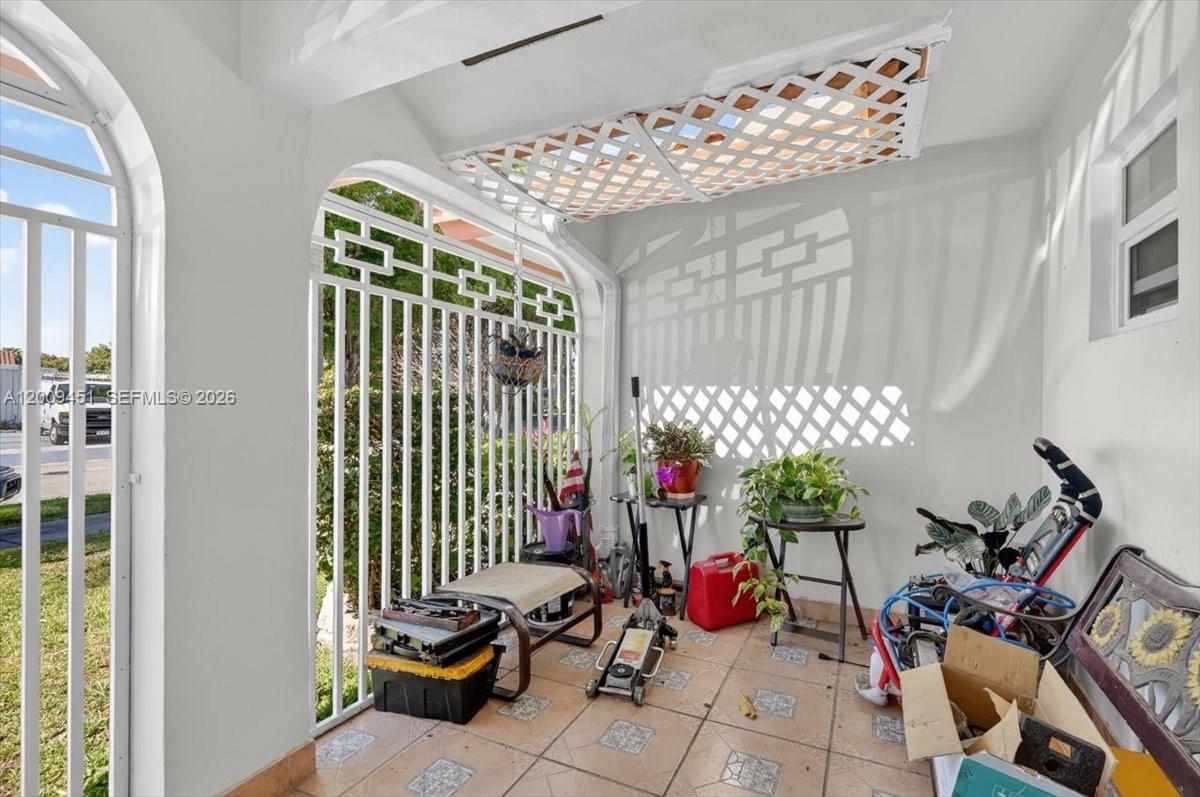 A covered outdoor patio features tiled flooring, white metal security bars, and lattice ceiling panels — 14313 SW 100th Ln, Miami FL 33186, MIAMI, FL