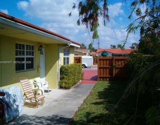 A yellow house exterior features a concrete walkway, two lawn chairs, and a wooden fence — 625 SW 3rd St, Hallandale Beach FL 33009, HALLANDALE BEACH, FL