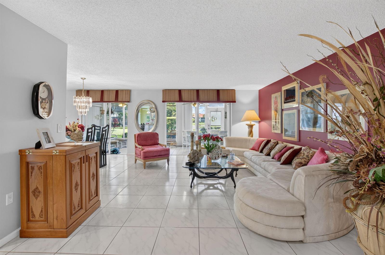 A spacious living room features white tile floors, a large sectional sofa, and red walls — 7825 Whispering Palms Drive # 101, Boynton Beach FL 33437, BOYNTON BEACH, FL