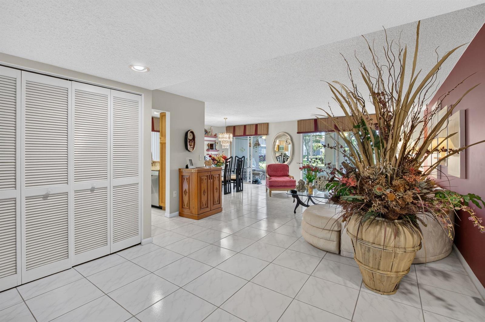 A spacious living and dining area features white tile flooring, louvered closet doors, and decor — 7825 Whispering Palms Drive # 101, Boynton Beach FL 33437, BOYNTON BEACH, FL