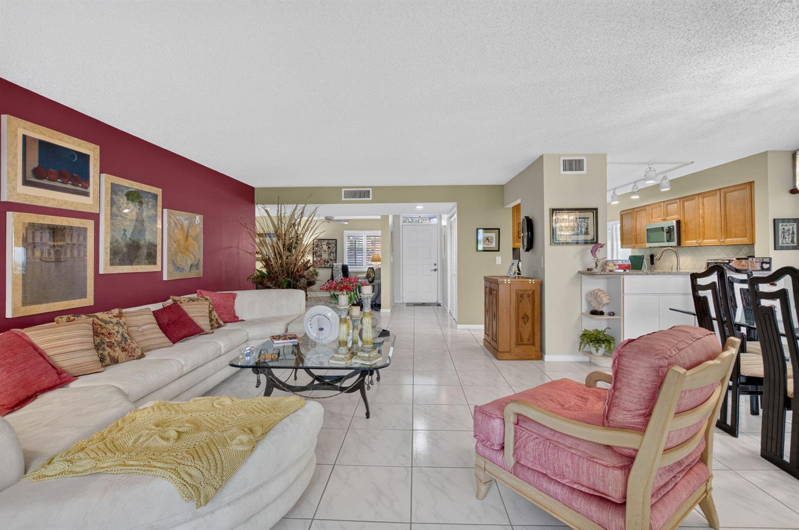A living room features a red accent wall, white sofa, tiled floors, and an open kitchen — 7825 Whispering Palms Drive # 101, Boynton Beach FL 33437, BOYNTON BEACH, FL