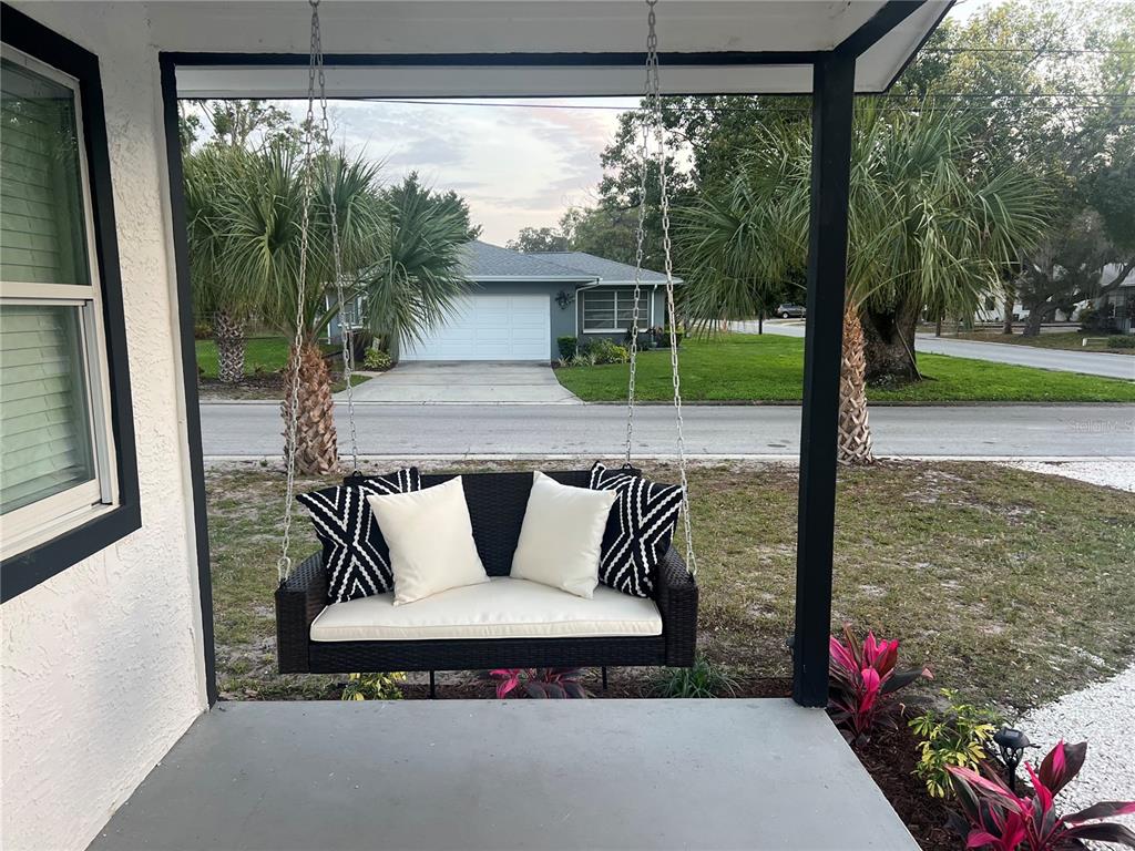 A black wicker porch swing with white and patterned pillows hangs on a covered porch — 1411 S MADISON AVENUE, CLEARWATER, FL
