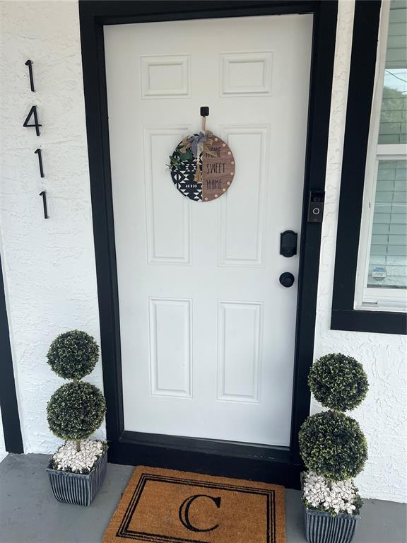 A white front door with a decorative sign and two topiary plants sits beside house numbers — 1411 S MADISON AVENUE, CLEARWATER, FL