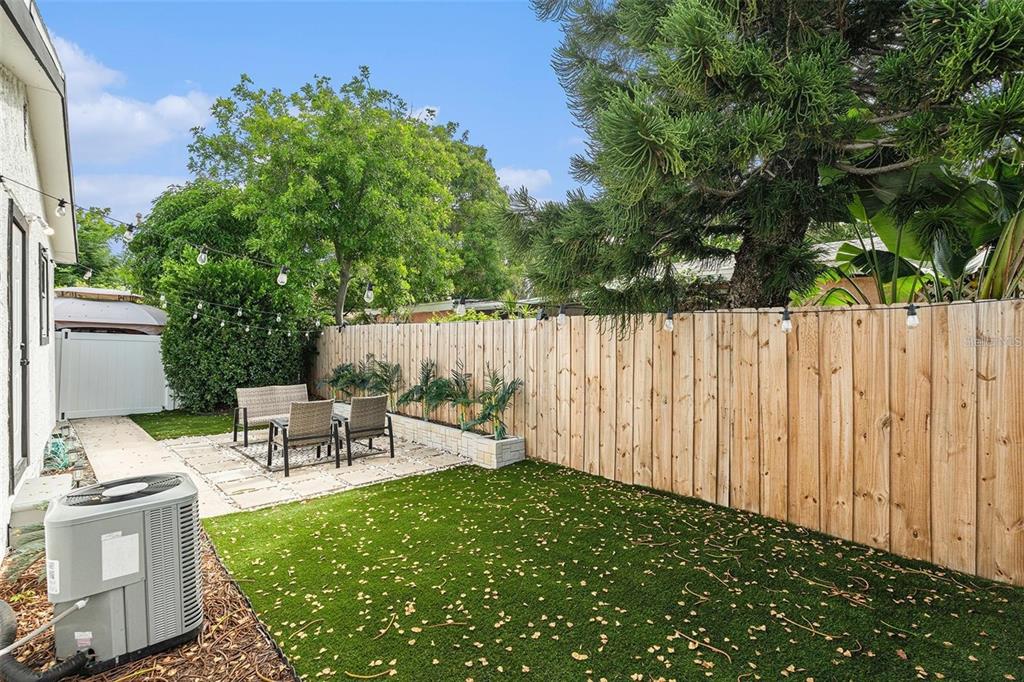 A fenced backyard features artificial turf, a stone patio with outdoor seating, and string lights — 1411 S MADISON AVENUE, CLEARWATER, FL