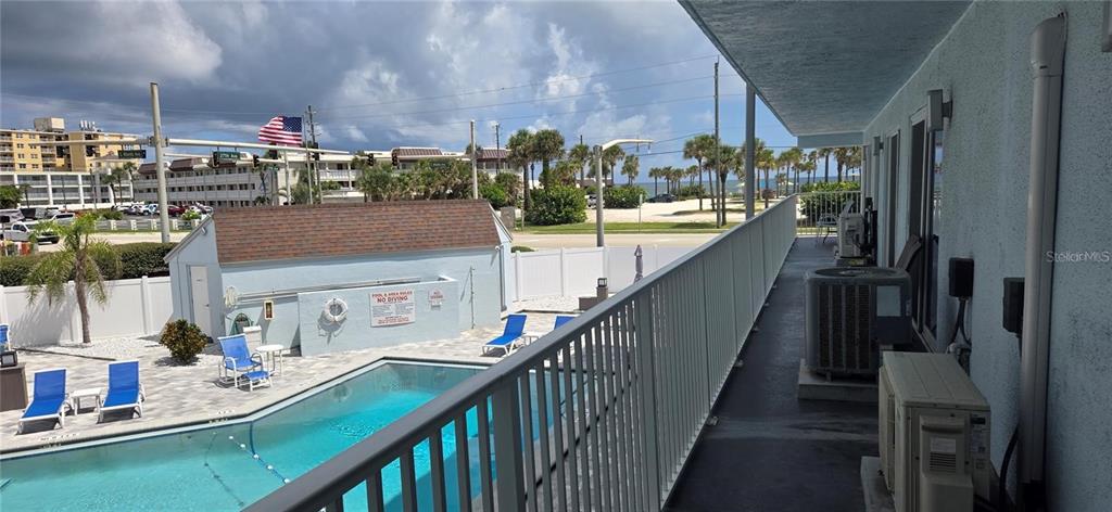 An elevated balcony overlooks a swimming pool and a nearby beach area — 3700 S ATLANTIC AVENUE UNIT 205, NEW SMYRNA BEACH, FL