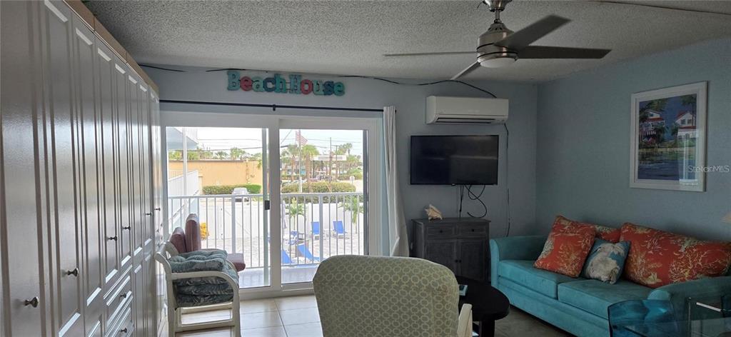 A living room features a teal sofa, a ceiling fan, and a sliding glass door — 3700 S ATLANTIC AVENUE UNIT 205, NEW SMYRNA BEACH, FL