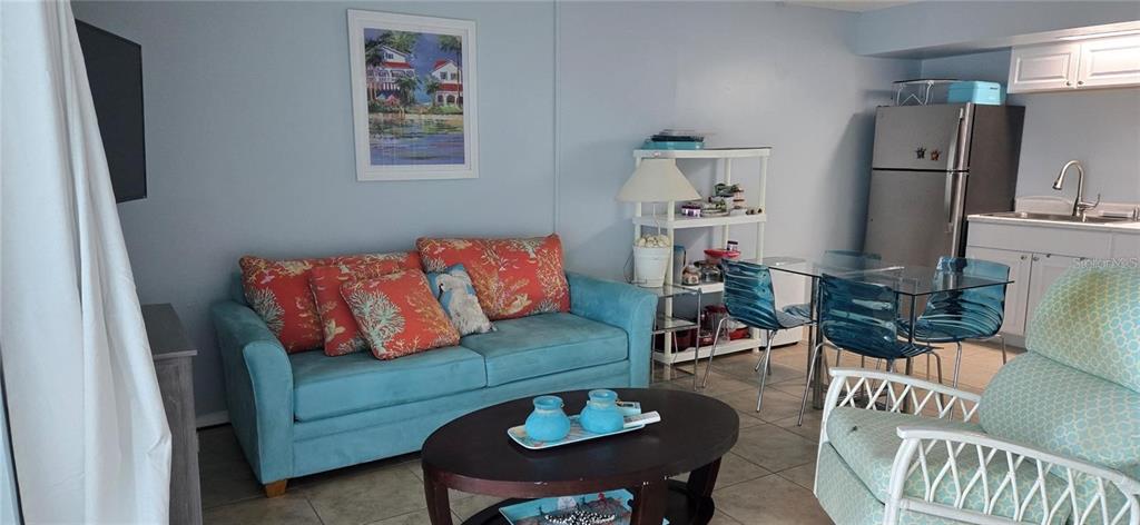 A living room features a blue sofa with coral pillows, a coffee table, and kitchenette — 3700 S ATLANTIC AVENUE UNIT 205, NEW SMYRNA BEACH, FL