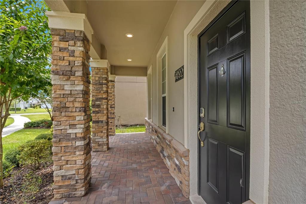A covered front porch features stone-clad columns, a brick paver floor, and a black front door — 9892 PECAN HICKORY WAY, ORLANDO, FL