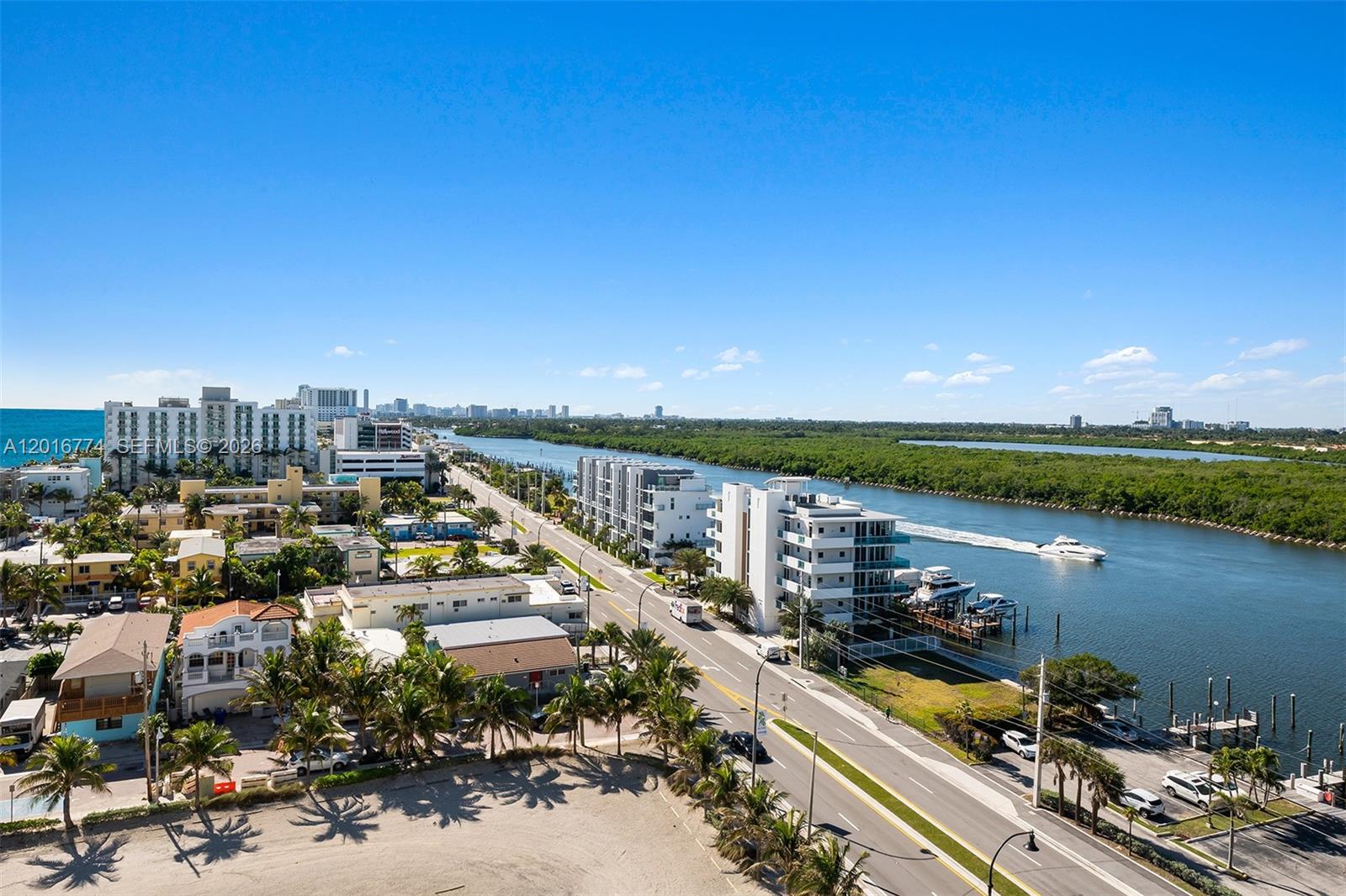 An aerial view shows a coastal road, residential buildings, and a boat traveling on a waterway — 3111 N Ocean Dr # 1110, Hollywood FL 33019, HOLLYWOOD, FL
