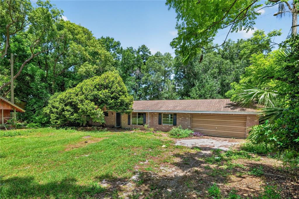 A single-story brick house with a two-car garage sits on a grassy, tree-filled lot — 320 LAKE MILLSITE ROAD, BARTOW, FL