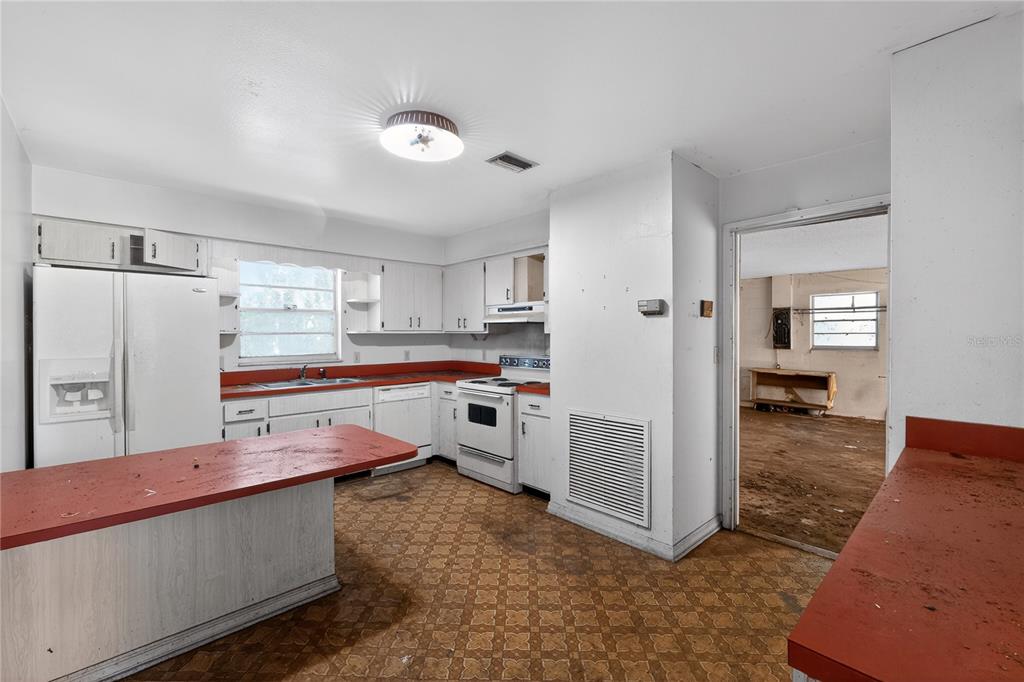 A kitchen with white cabinets, red countertops, and patterned flooring leads into an unfinished room — 320 LAKE MILLSITE ROAD, BARTOW, FL