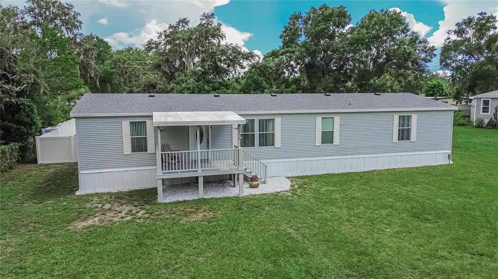 A light gray manufactured home with a front porch sits on a grassy lot — 38310 PEAR COURT, ZEPHYRHILLS, FL
