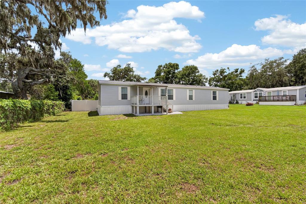 A light gray manufactured home sits on a large grassy lot under a blue sky — 38310 PEAR COURT, ZEPHYRHILLS, FL