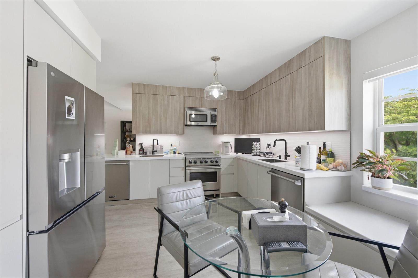 A modern kitchen features light wood cabinets, stainless steel appliances, white countertops, and a glass table — 7369 Orangewood Lane, Boca Raton FL 33433, BOCA RATON, FL